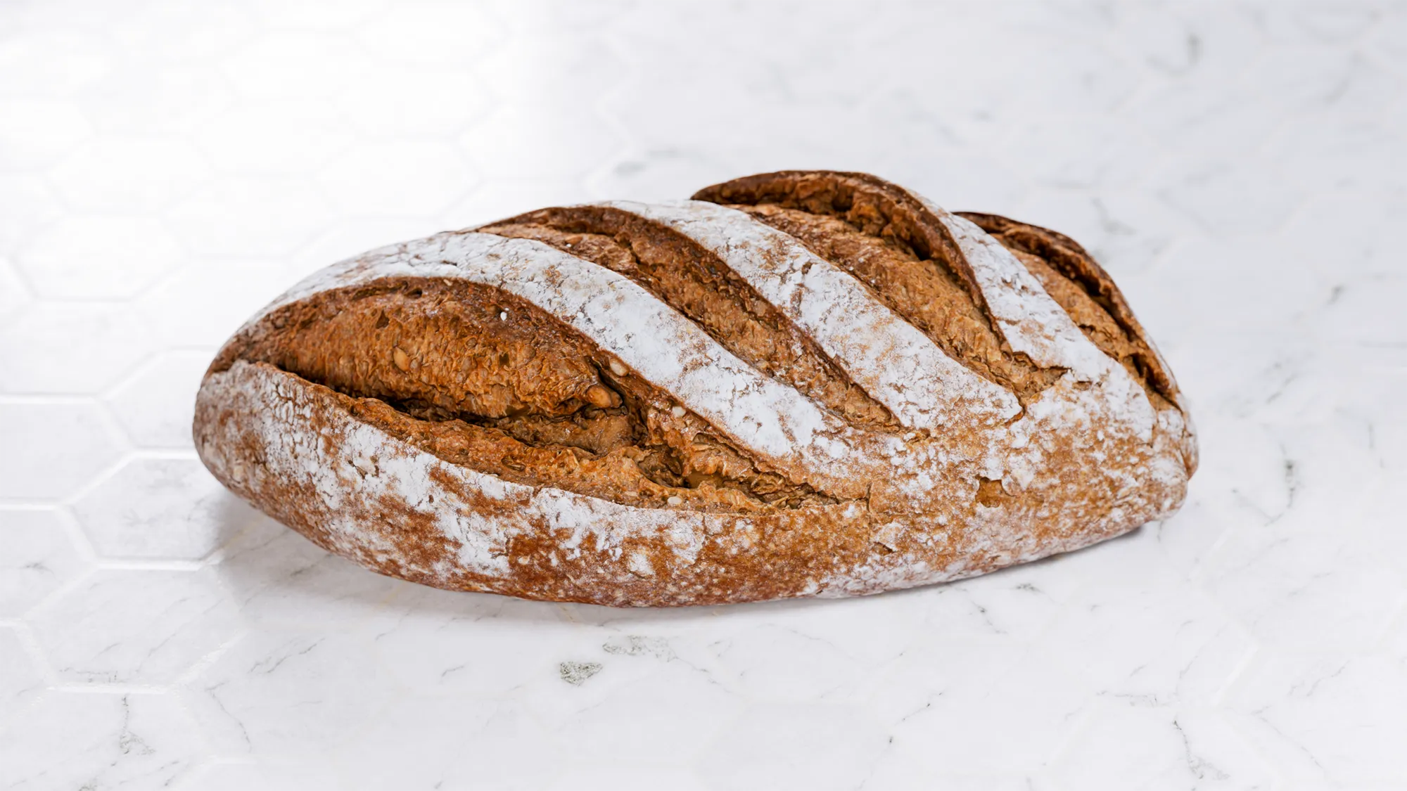 Loaf of bread with a rustic crust on a white marble surface