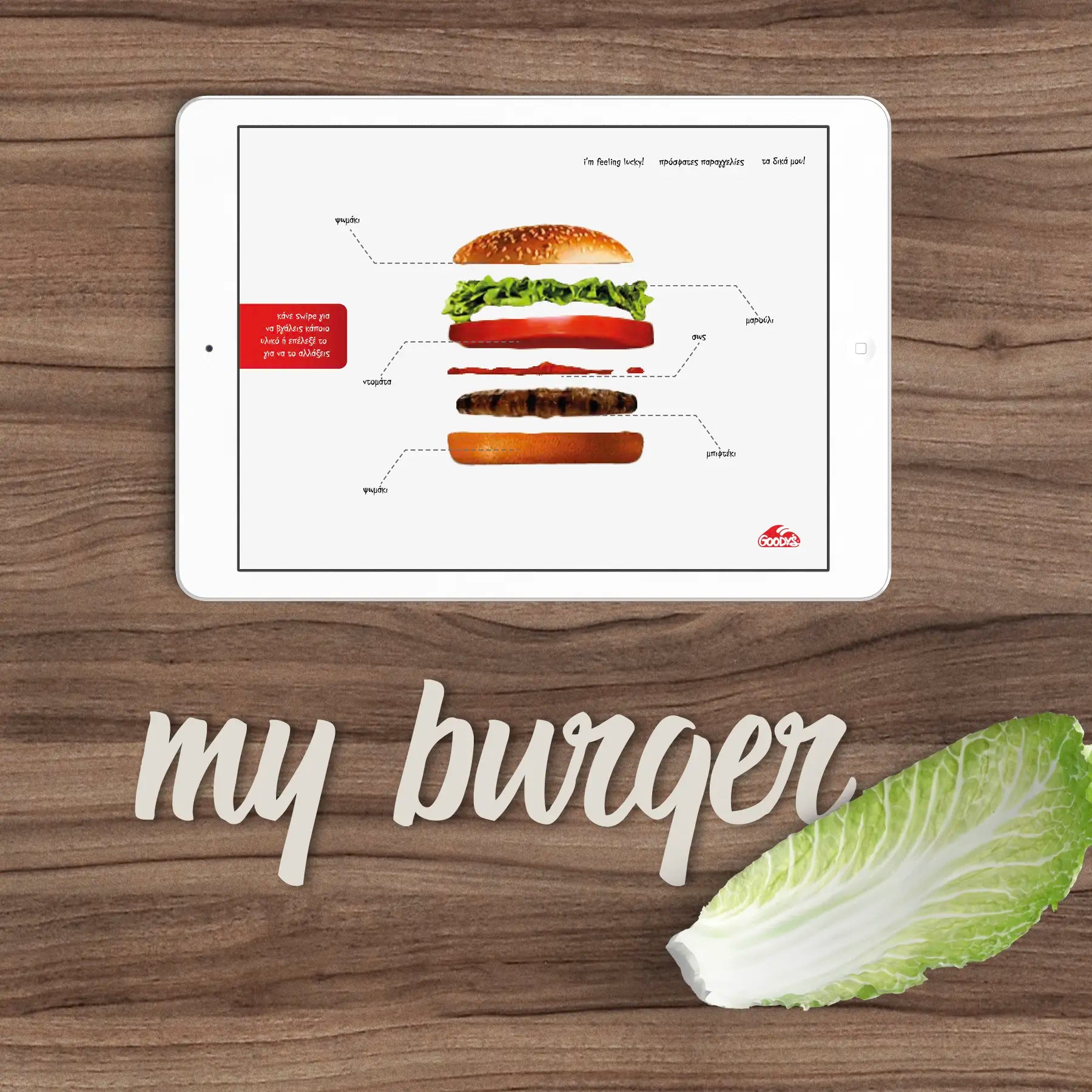 Tablet displaying a burger assembly diagram on a wooden surface with a leaf of lettuce.