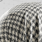Close-up of a textured fabric with a houndstooth pattern on a white background.